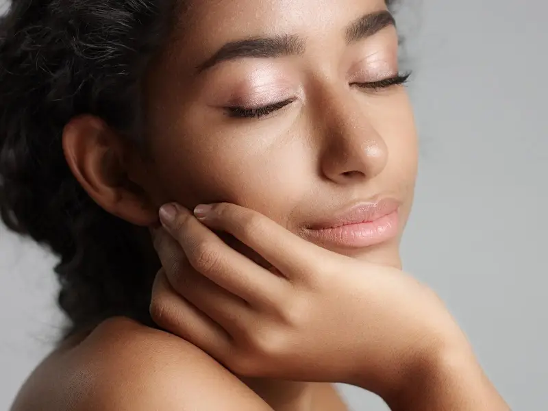 Happy serene young woman with beautiful olive skin and curly hair ideal skin and brown eyes in studio